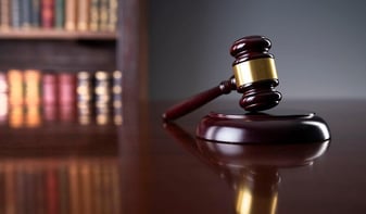 Alt text: A judge’s gavel rests on a wooden desk in a courtroom, with law books blurred in the background, symbolizing justice and legal authority.