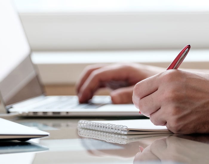 person typing on computer and writing in notebook